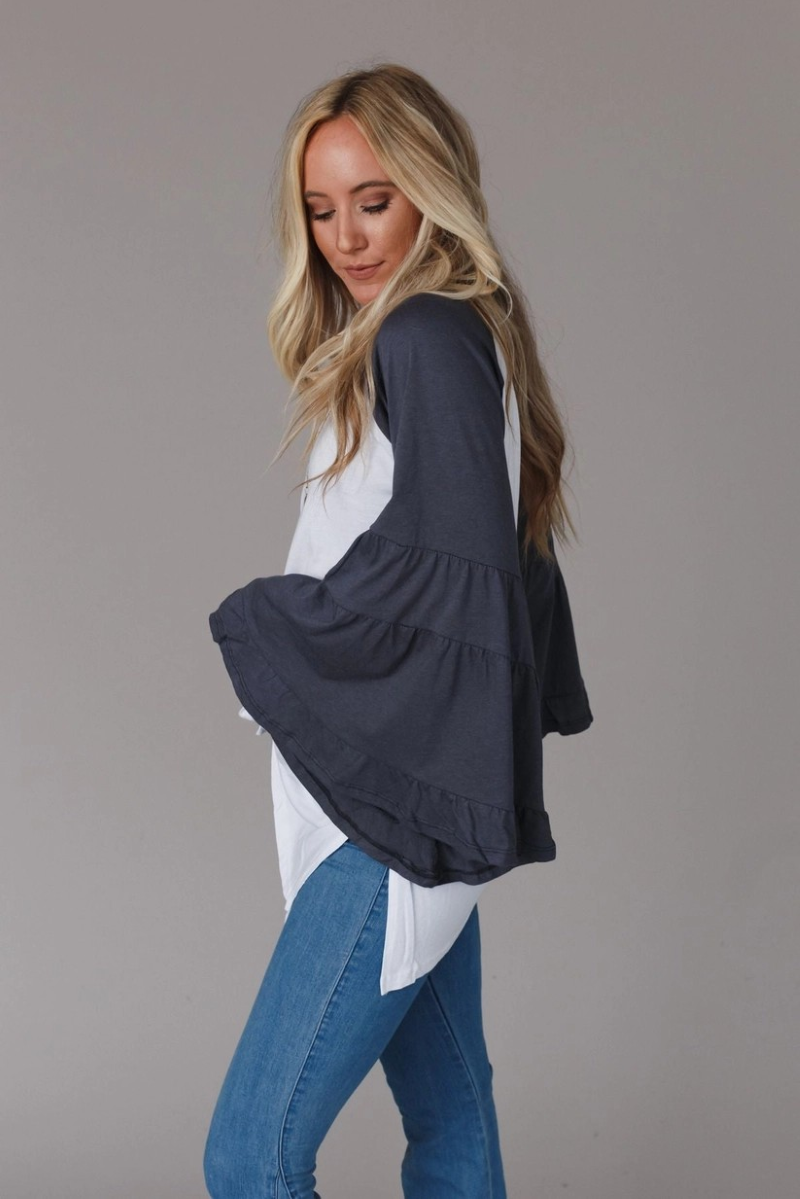 Woman wearing baseball tee with charcoal flounce sleeves and jeans on a gray background