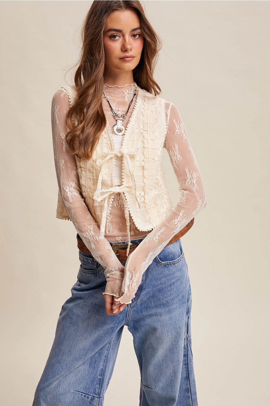 Woman wearing a sheer lace top and blue jeans against a beige background