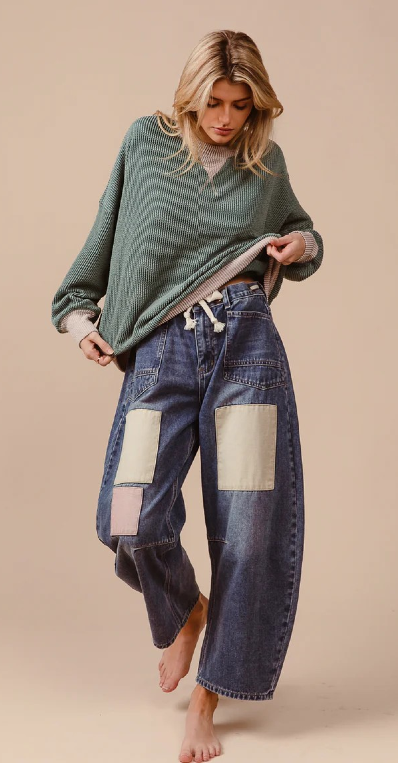 Woman wearing patchwork jeans barefoot with a green shirt on a beige background