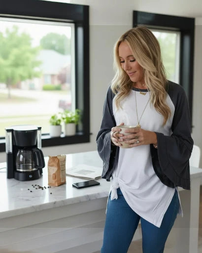 Woman holding a mug in a kitchen with a coffee maker and laptop on the counter.