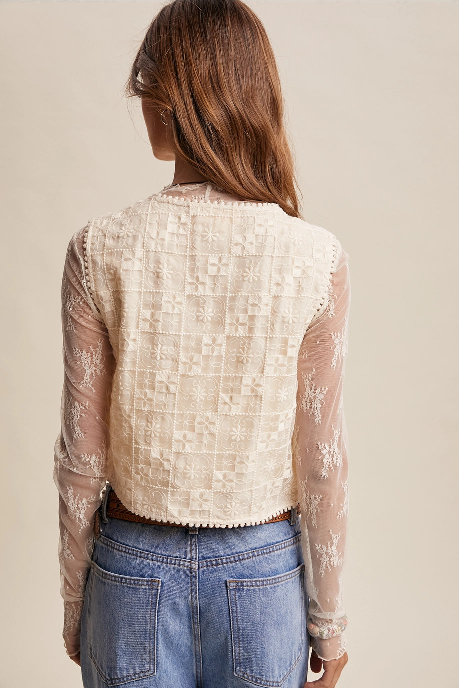 Person wearing a beige lace top with sheer sleeves against a neutral background